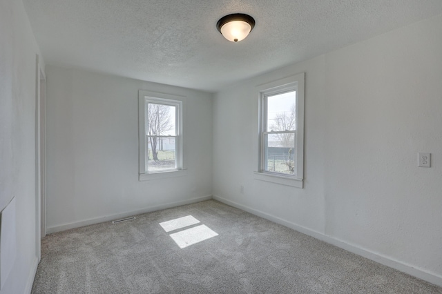 carpeted spare room featuring visible vents, baseboards, and a textured ceiling