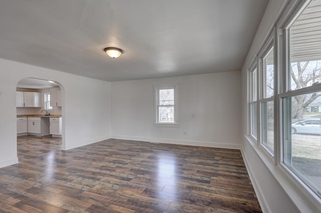 unfurnished room featuring baseboards, arched walkways, dark wood-style flooring, and a sink