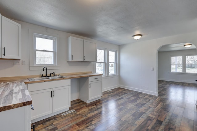 kitchen featuring visible vents, arched walkways, dark wood-style flooring, a sink, and wood counters