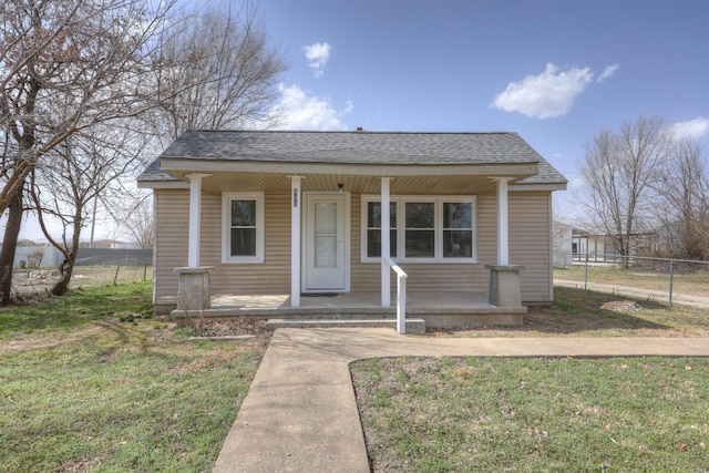 bungalow-style home with fence, covered porch, a front yard, and a shingled roof