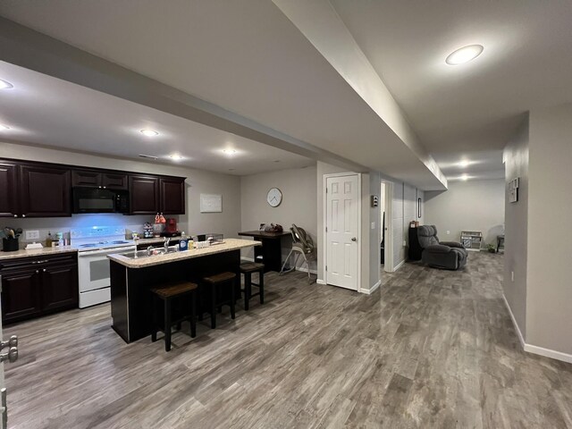610 N Center St, Willow Springs, MO 65793 - kitchen with black microwave, a center island with sink, a breakfast bar, wood finished floors, and electric range