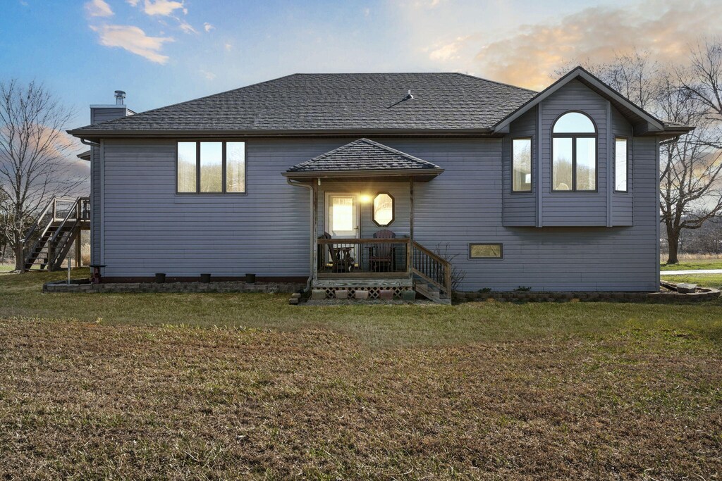 rear view of property featuring a lawn, a chimney, and a shingled roof