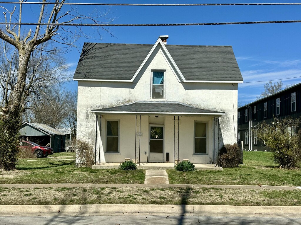 view of front of home with stucco siding, a front lawn, roof with shingles, covered porch, and a chimney