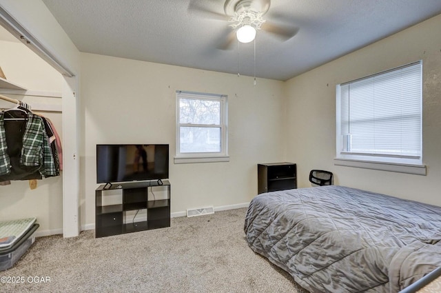 carpeted bedroom featuring ceiling fan, baseboards, visible vents, and a textured ceiling