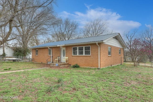 ranch-style home with metal roof, brick siding, a front yard, and fence