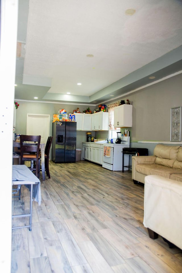 kitchen with open floor plan, light wood-style floors, white range with electric stovetop, black fridge with ice dispenser, and white cabinets