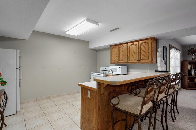 304 Reavley Dr, Lamar, MO 64759 - kitchen with white appliances, visible vents, a breakfast bar, a peninsula, and brown cabinets