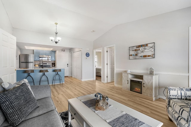 living area with baseboards, light wood finished floors, lofted ceiling, a glass covered fireplace, and a notable chandelier