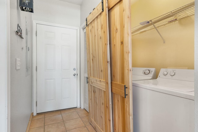 clothes washing area featuring a barn door, light tile patterned flooring, and washing machine and dryer
