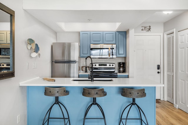 kitchen featuring a kitchen breakfast bar, blue cabinets, appliances with stainless steel finishes, and a sink