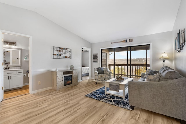 living room with a glass covered fireplace, vaulted ceiling, baseboards, and light wood-type flooring