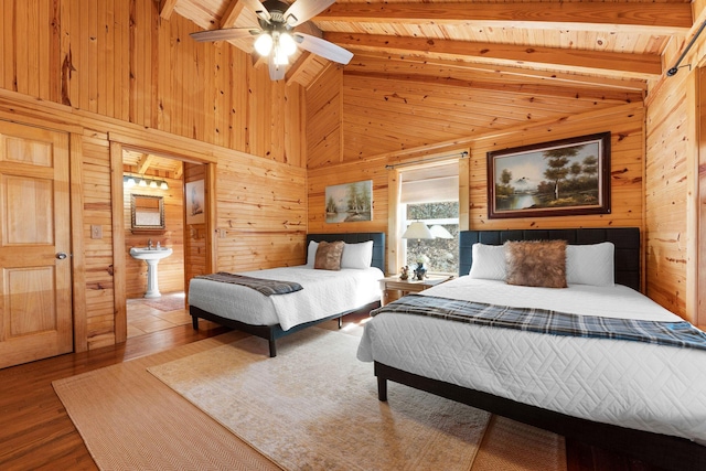 bedroom with wooden walls, ceiling fan, lofted ceiling with beams, wood finished floors, and ensuite bath
