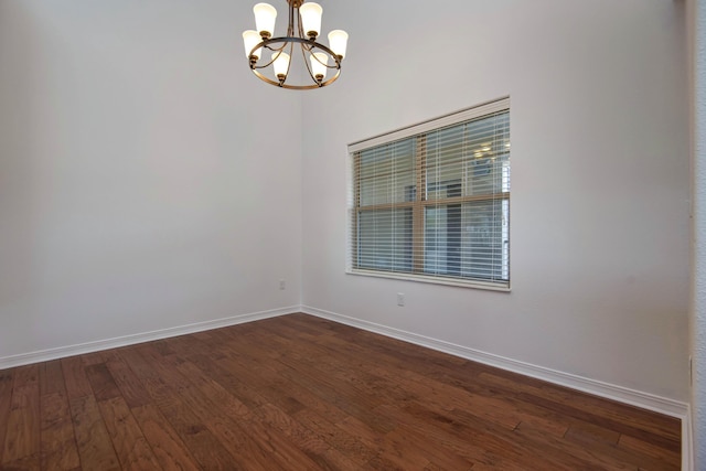 spare room with dark wood-style floors, baseboards, and a chandelier