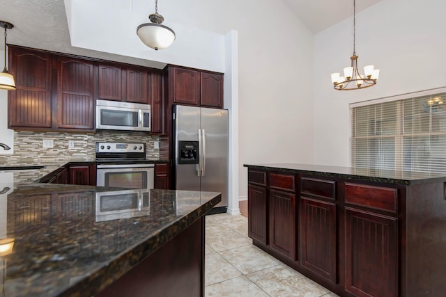 kitchen featuring dark stone counters, decorative backsplash, appliances with stainless steel finishes, an inviting chandelier, and a sink