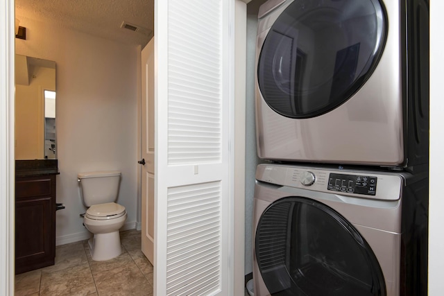 laundry room with stacked washer / dryer, visible vents, light tile patterned floors, laundry area, and a textured ceiling