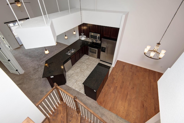 kitchen with dark countertops, baseboards, ceiling fan with notable chandelier, appliances with stainless steel finishes, and light wood-style flooring