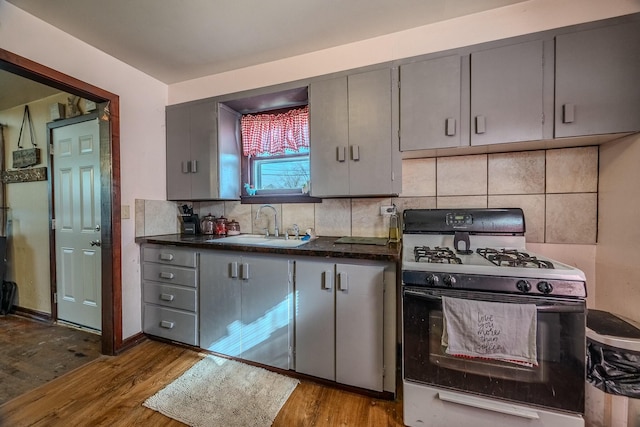 kitchen featuring gas stove, decorative backsplash, wood finished floors, and a sink