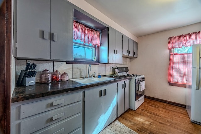 kitchen featuring gray cabinetry, a sink, tasteful backsplash, white appliances, and light wood-style floors
