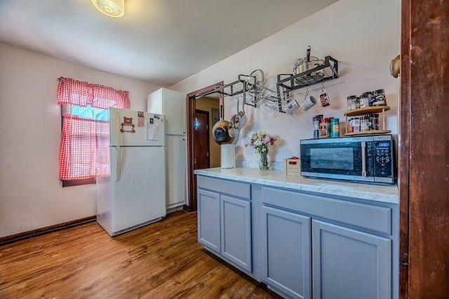 kitchen with stainless steel microwave, baseboards, light countertops, freestanding refrigerator, and wood finished floors