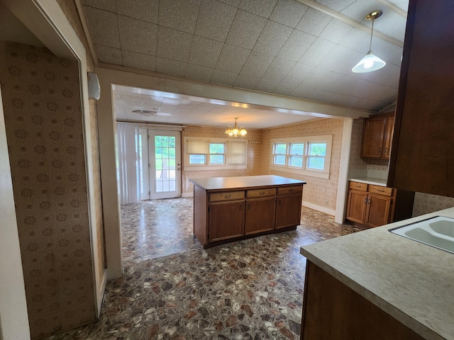 1622 W Fairview Ave, Carthage, MO 64836 - kitchen with wallpapered walls, a chandelier, a kitchen island, brown cabinetry, and hanging light fixtures