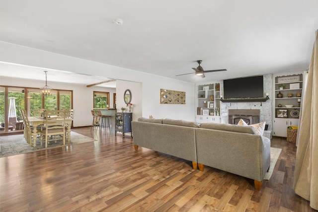 living area featuring ceiling fan with notable chandelier, built in shelves, wood finished floors, and a fireplace
