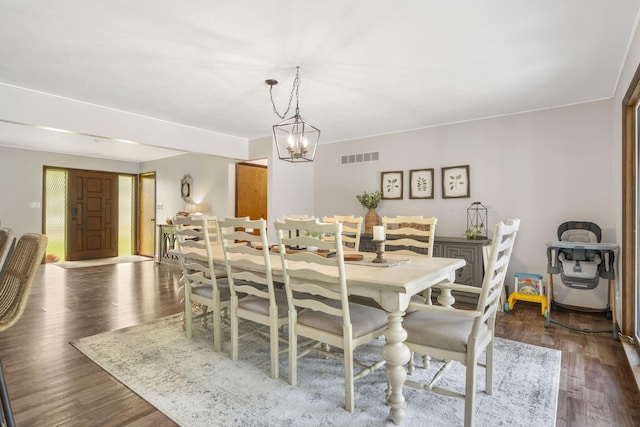 dining space with dark wood-type flooring, visible vents, and an inviting chandelier