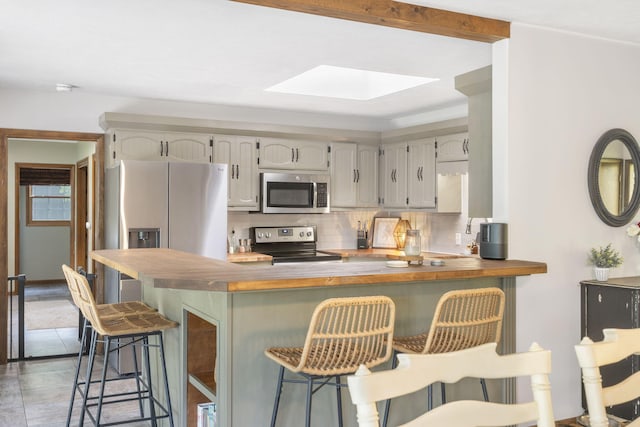 kitchen featuring a peninsula, a skylight, appliances with stainless steel finishes, a breakfast bar area, and backsplash