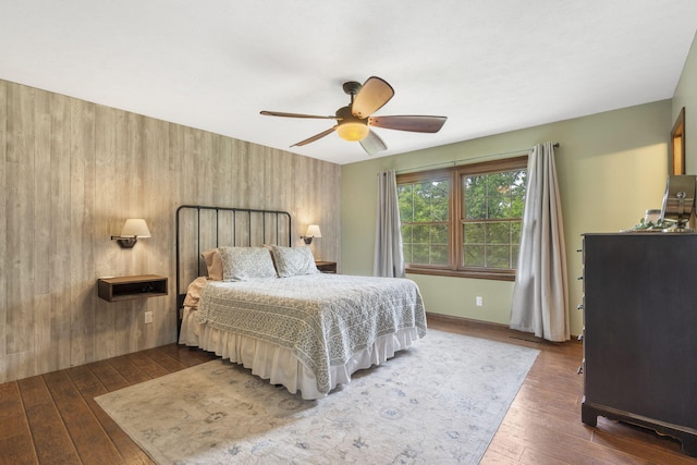 bedroom featuring wooden walls, baseboards, a ceiling fan, and hardwood / wood-style floors