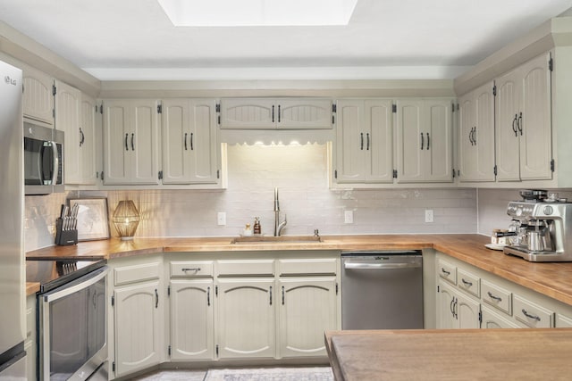 kitchen with a sink, wood counters, stainless steel appliances, backsplash, and a skylight