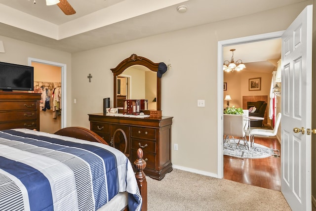 carpeted bedroom with ceiling fan with notable chandelier, baseboards, and a walk in closet