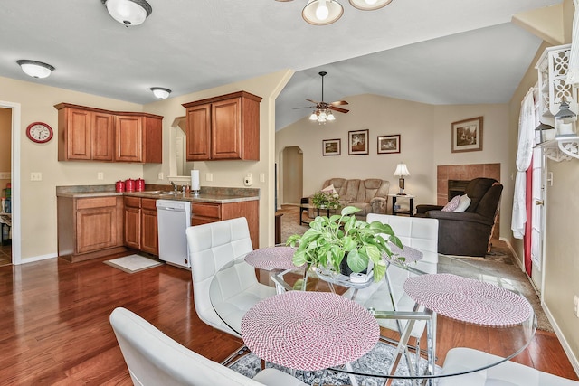 dining area with baseboards, ceiling fan, dark wood-style floors, vaulted ceiling, and a tile fireplace