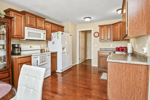kitchen featuring brown cabinetry, white appliances, dark wood-style floors, and a sink