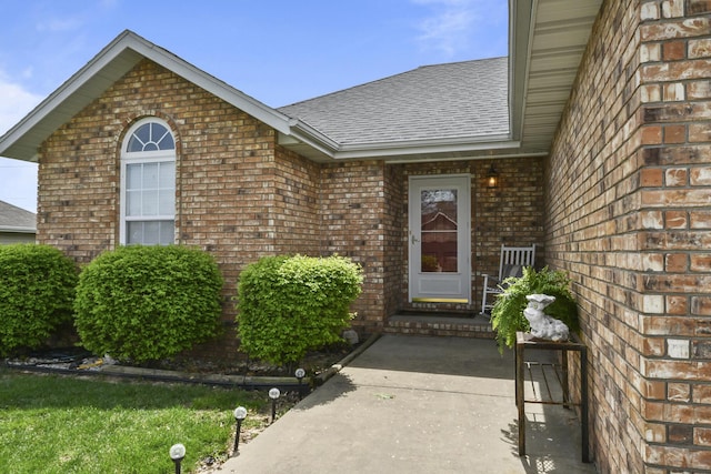 view of exterior entry with brick siding and roof with shingles
