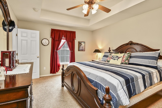 carpeted bedroom with baseboards, a raised ceiling, and a ceiling fan