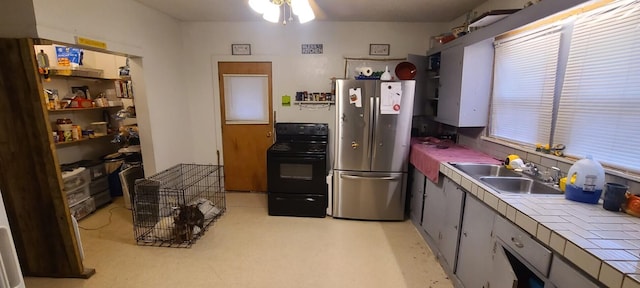kitchen featuring tile counters, black electric range, freestanding refrigerator, and a sink