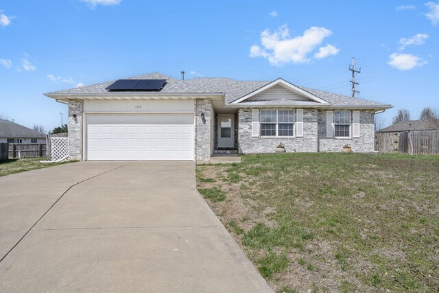 single story home featuring solar panels, an attached garage, fence, and driveway