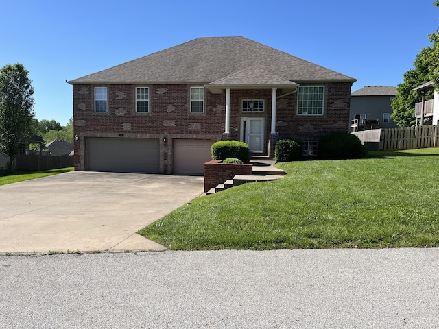 raised ranch featuring brick siding, concrete driveway, an attached garage, and fence
