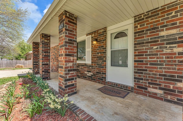 property entrance with brick siding, fence, and a porch
