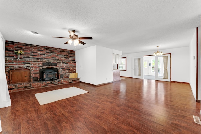 unfurnished living room with a textured ceiling, baseboards, ceiling fan with notable chandelier, wood finished floors, and a wood stove
