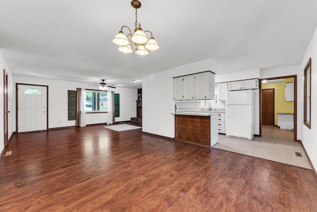 unfurnished living room featuring wood finished floors, visible vents, baseboards, and ceiling fan with notable chandelier