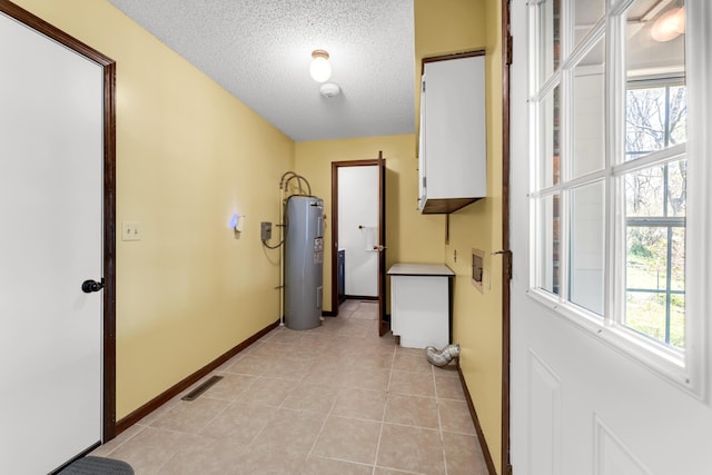 corridor featuring baseboards, electric water heater, a textured ceiling, and light tile patterned floors