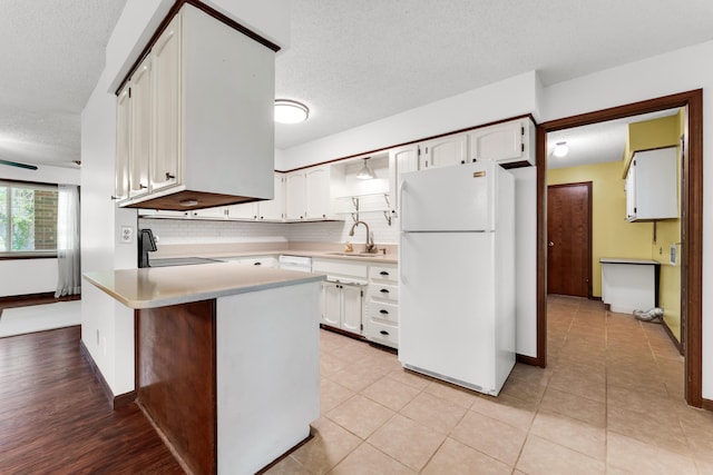 kitchen with white cabinets, a peninsula, a textured ceiling, freestanding refrigerator, and light countertops