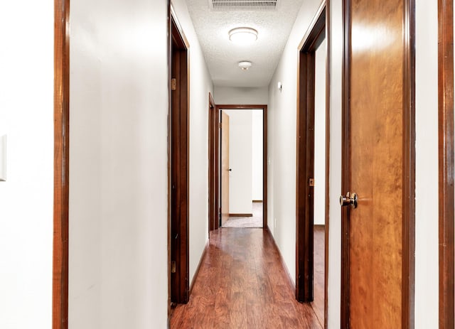 corridor featuring baseboards, a textured ceiling, dark wood-style floors, and visible vents