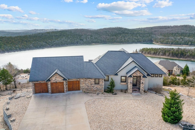 view of front of property with a view of trees, an attached garage, stone siding, and a water view