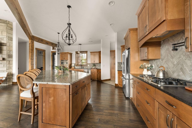 kitchen featuring a kitchen breakfast bar, a kitchen island, brown cabinets, decorative backsplash, and appliances with stainless steel finishes