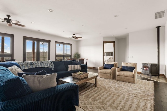 living room with a wood stove, ceiling fan, visible vents, and dark wood-style floors