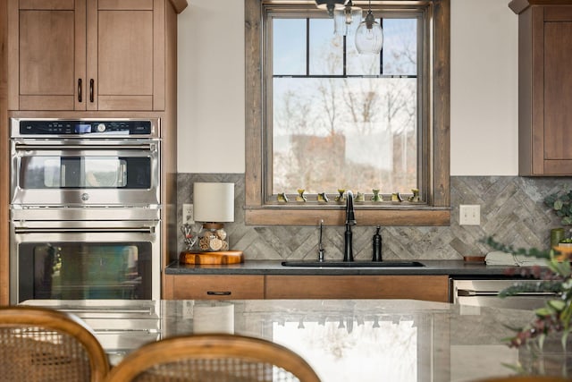 kitchen with brown cabinetry, decorative backsplash, a sink, and double oven