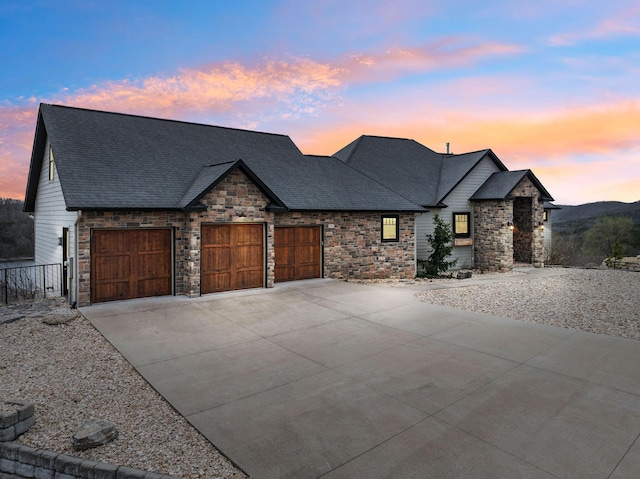 view of front of home featuring an attached garage, a shingled roof, stone siding, and concrete driveway