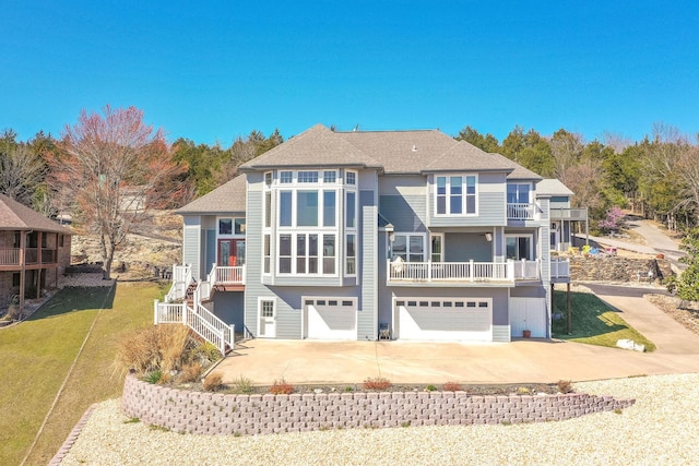view of front facade with an attached garage, concrete driveway, stairway, a front lawn, and a shingled roof