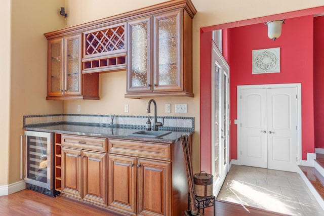 bar featuring light wood-style flooring, baseboards, wine cooler, and a sink